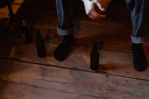 Free A person in denim and black socks sits on a wooden floor surrounded by beer bottles, reflecting a contemplative atmosphere. Stock Photo