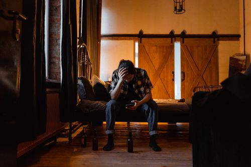 Free A man sits on a bed in a dark room, appearing pensive and stressed. Stock Photo
