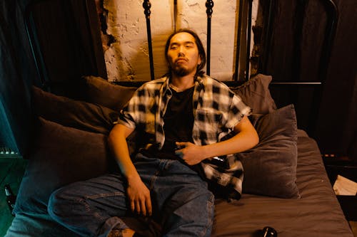 無料 白と黒の格子縞のボタンアップシャツとソファに座っている青いデニムジーンズの男 写真素材