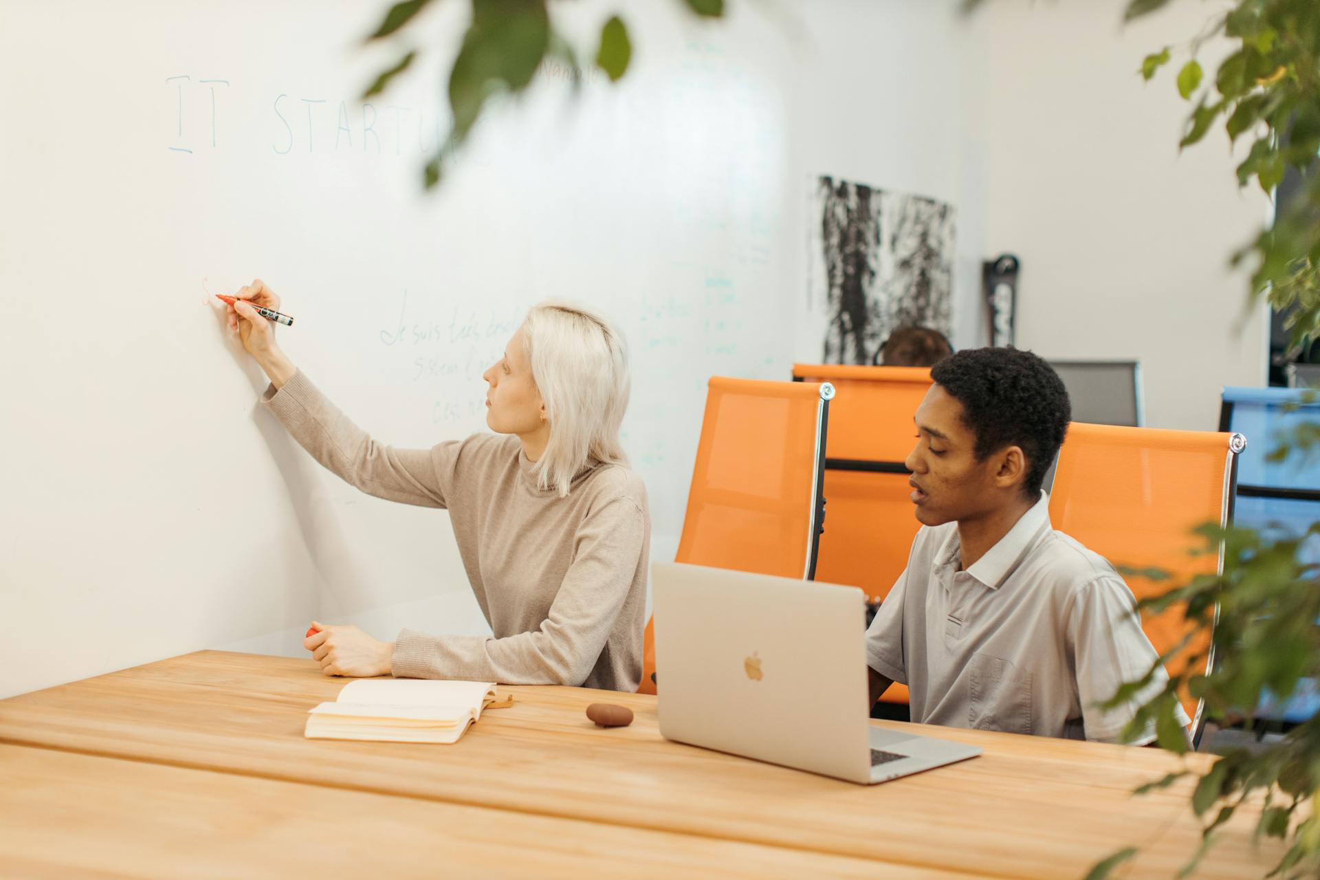 Two professionals collaborating at a startup office with a whiteboard and laptop.