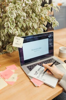 A creative workspace featuring a laptop and handwritten notes for a business plan.