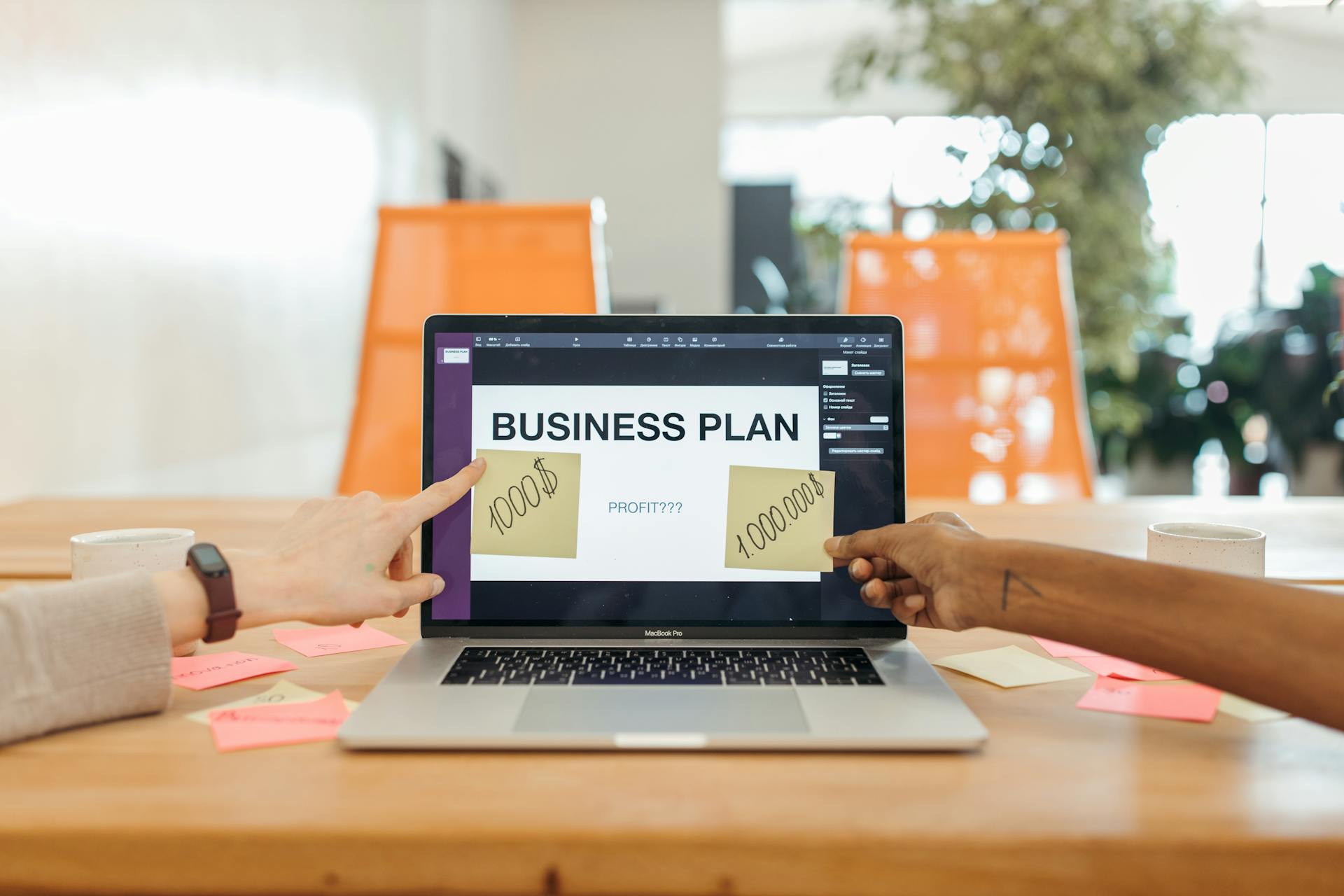 Two professionals strategizing a business plan on a laptop with sticky notes and profit goals.