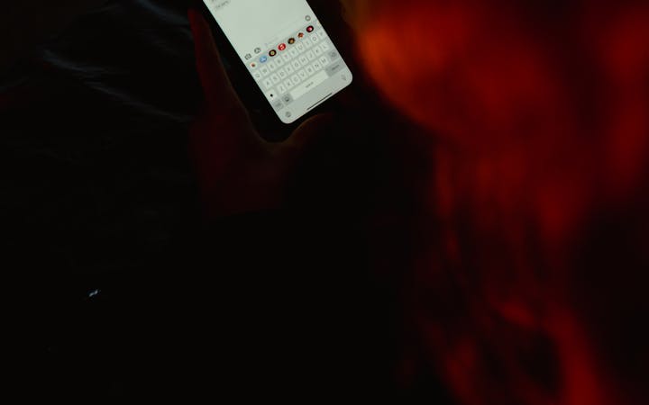A person texting on a smartphone in a dark room with red lighting.