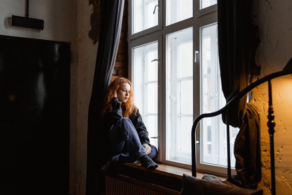 Person sitting quietly by a window feeling anxious and thoughtful