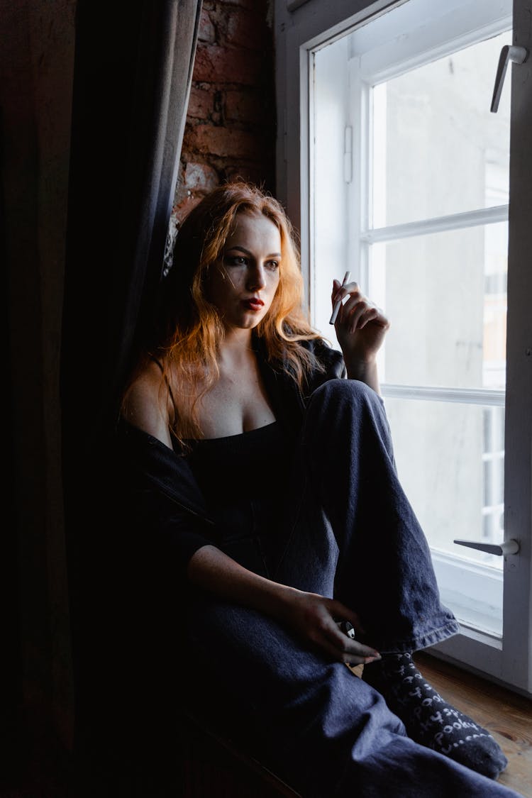 Sad Woman Sitting By The Window While Holding A Cigarette