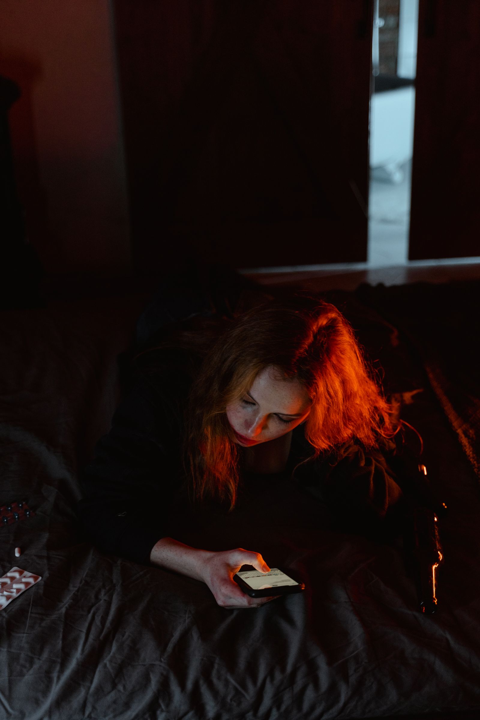 Young woman looking at her smartphone while lying on a bed in a dim room