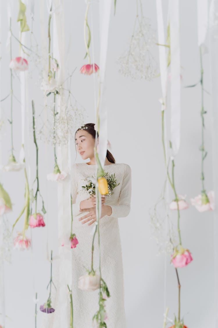 Woman Wearing A Wedding Dress, Posing In A Space With Hanging Flowers Installation