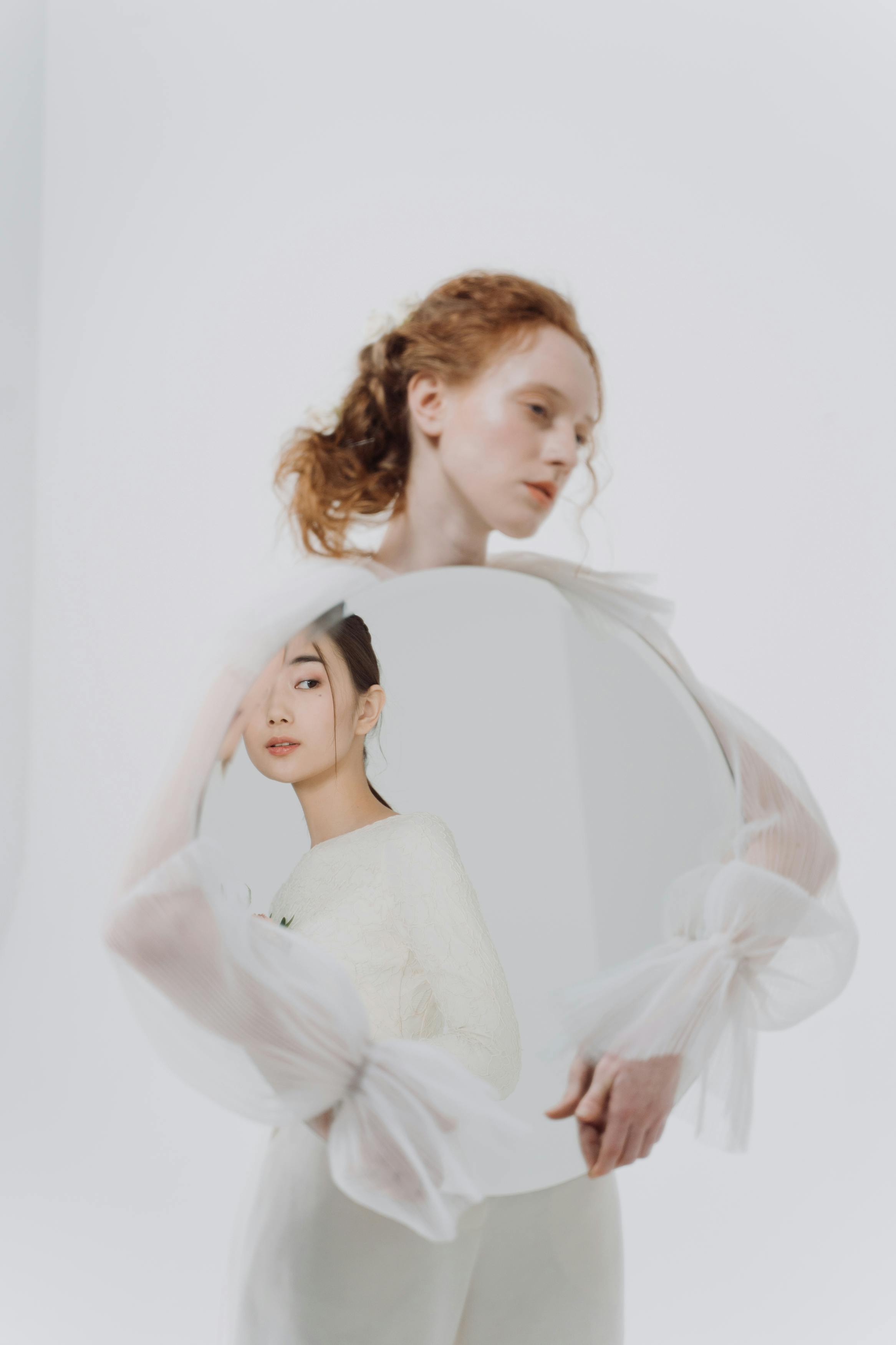 A conceptual portrait featuring a woman holding a mirror reflecting another woman, creating a surreal artistic effect.