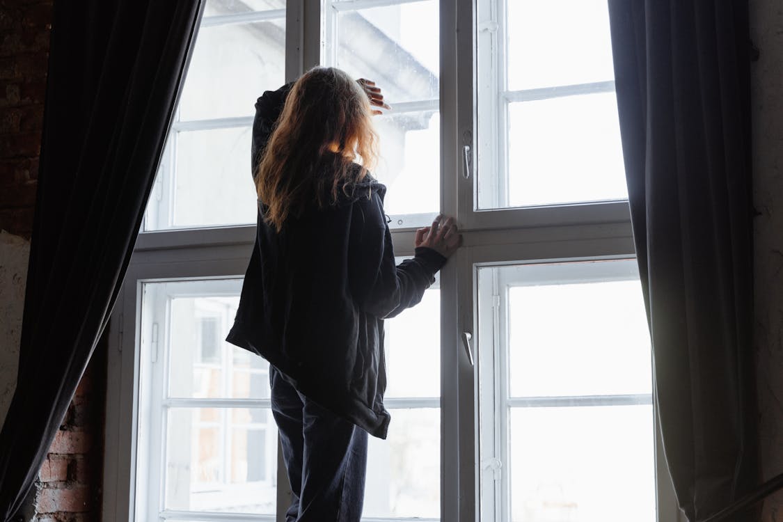 Free Back View of a Woman Standing while Looking through Window  Stock Photo