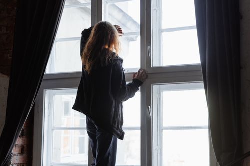 Free A woman stands by a window, lost in thought, with natural light streaming in. Stock Photo