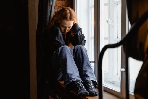 Free A woman sits pensively by a window, expressing feelings of solitude and contemplation. Stock Photo