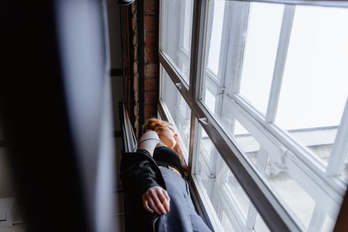 Free An adult woman leans against a window, lost in thought, indoors. Stock Photo