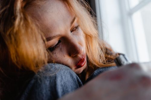 Free Close-up of a woman with red hair in a thoughtful and emotional moment indoors. Stock Photo