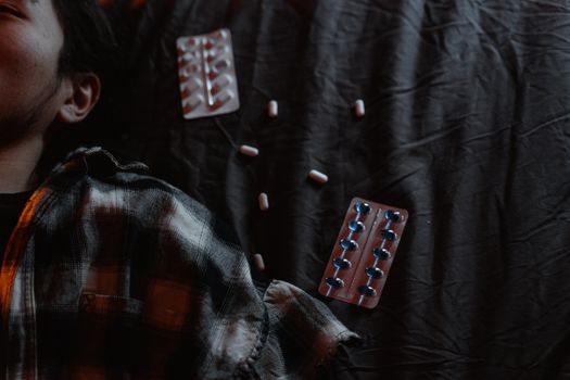 Moody portrait of a man lying next to scattered tablets, expressing distress.