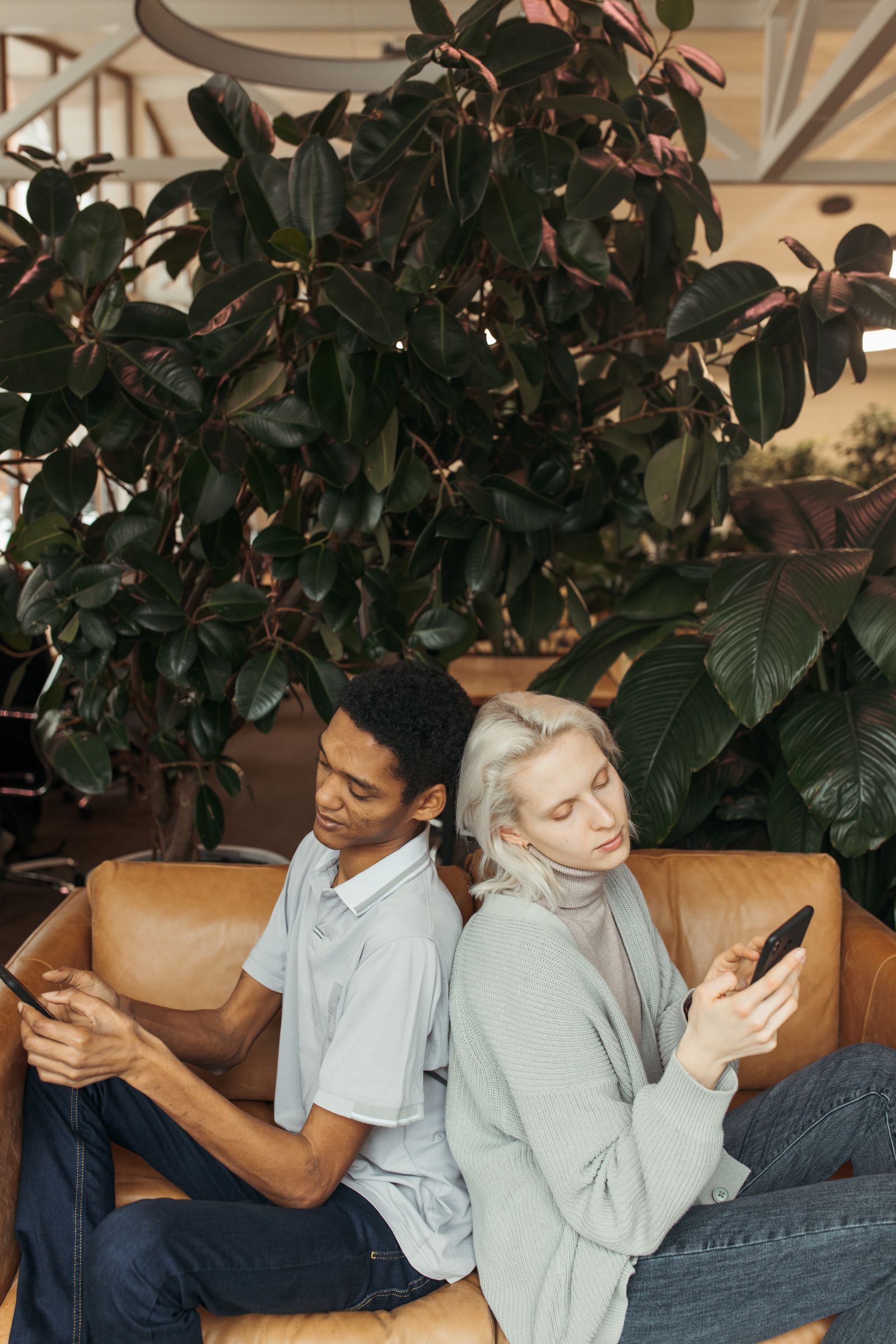Couple sitting back-to-back on a couch, each absorbed in their own phone