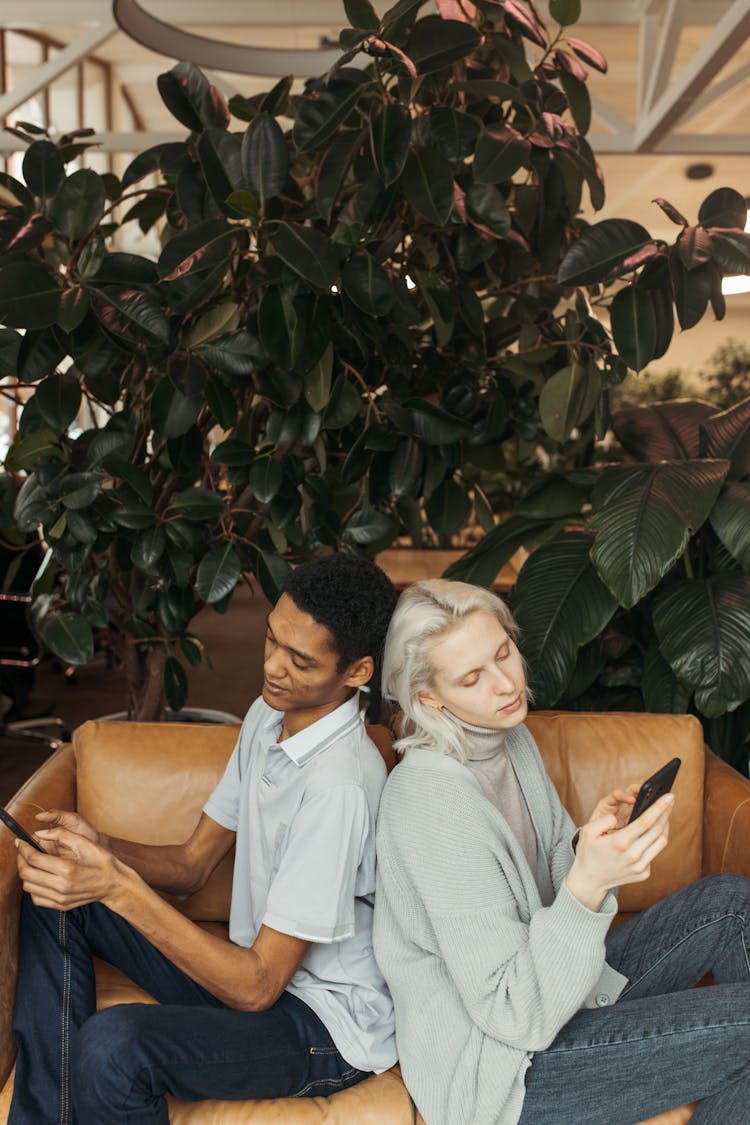 Man And Woman Sitting Back To Back On Brown Leather Couch