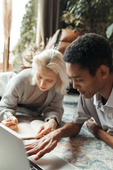 Two colleagues brainstorming ideas on the floor with a laptop and notebook in a serene workspace.
