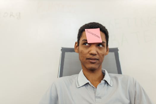 A young businessman with a 'Businessman' note on his forehead in a modern office setting.