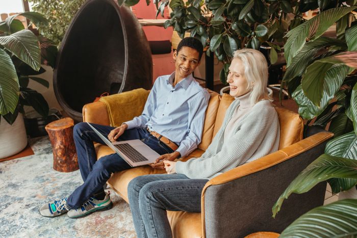 Two colleagues laughing over a laptop on a leather sofa — photo by Anastasia Shuraeva on Pexels
