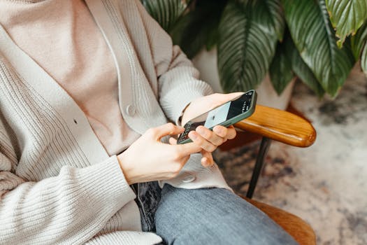 Close-up of a person sitting indoors using a smartphone with lush greenery in the background.