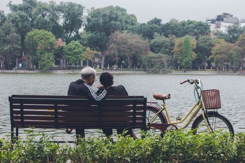 Free An elderly couple sits by a serene lake in Hanoi, embracing nature and tranquility. Stock Photo