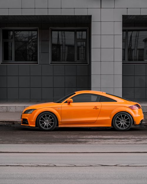 Free An orange coupe car parked on a city street against a modern building facade. Stock Photo