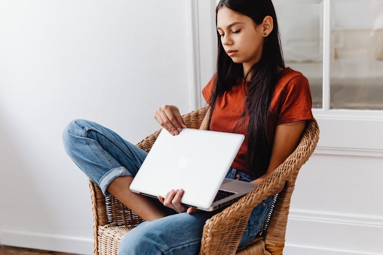 Teenage Girl Sitting On Chair While Holding A Laptop