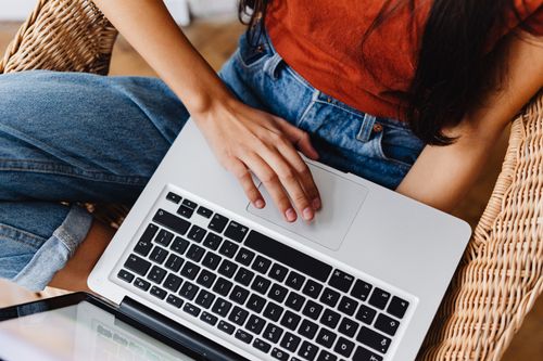 Free Close-up of a woman using a laptop indoors, seated on a wicker chair. Stock Photo
