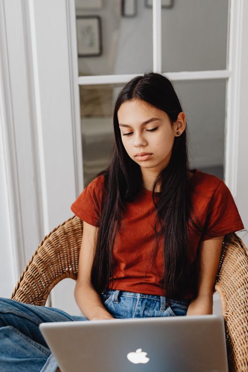 Free Teenager sitting in a chair using a laptop, relaxed home environment. Stock Photo