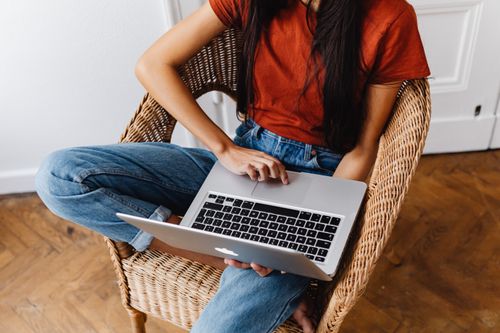 Free Young woman sitting on wicker chair using a laptop indoors, focusing on work. Stock Photo