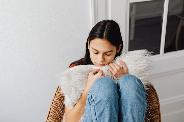 A Woman Sitting On A Chair Hugging A Furry Pillow