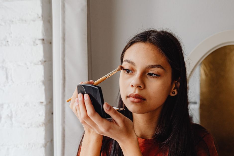 A focused young woman applying eyeshadow with a makeup brush indoors.