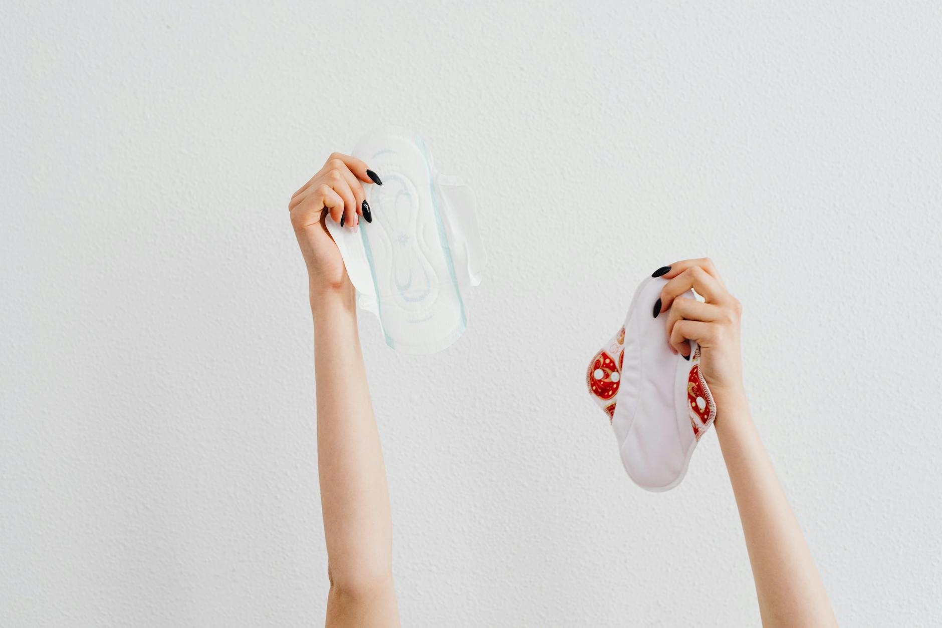 Female hands holding reusable and disposable sanitary pads on a white background.