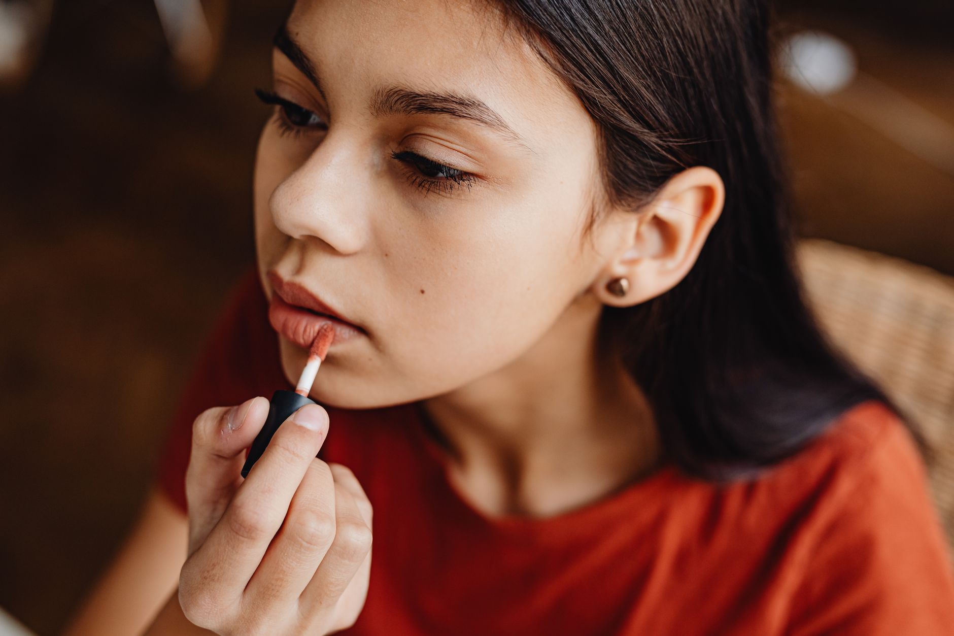 A close-up shot of a teenage girl applying lipstick indoors, focusing on a beauty routine.