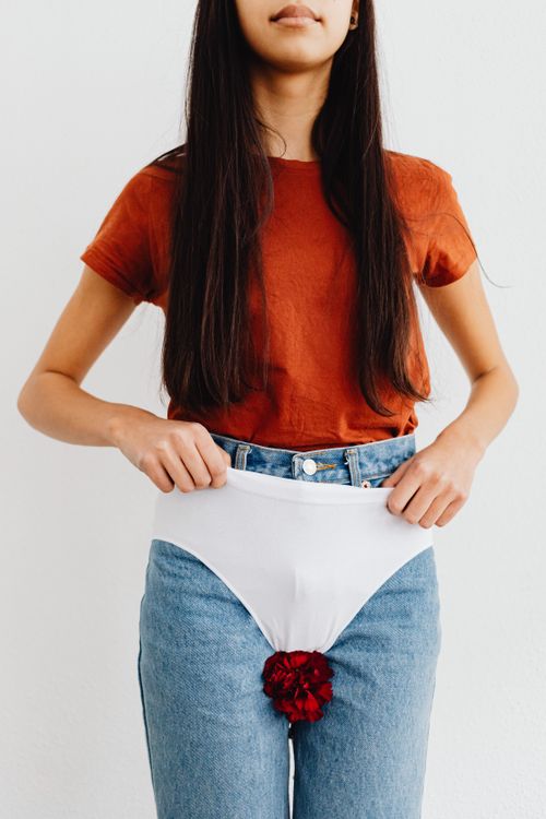Free Portrait of a young woman in jeans and t-shirt holding underwear with a red flower against a white background. Stock Photo