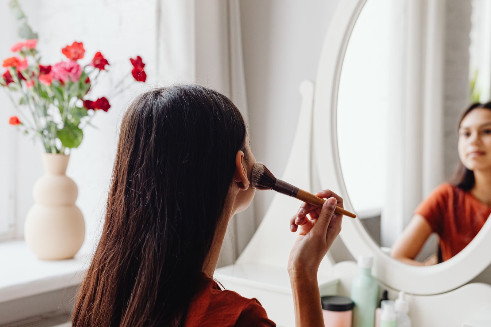 Woman applying foundation with a brush while checking the finish in a mirror