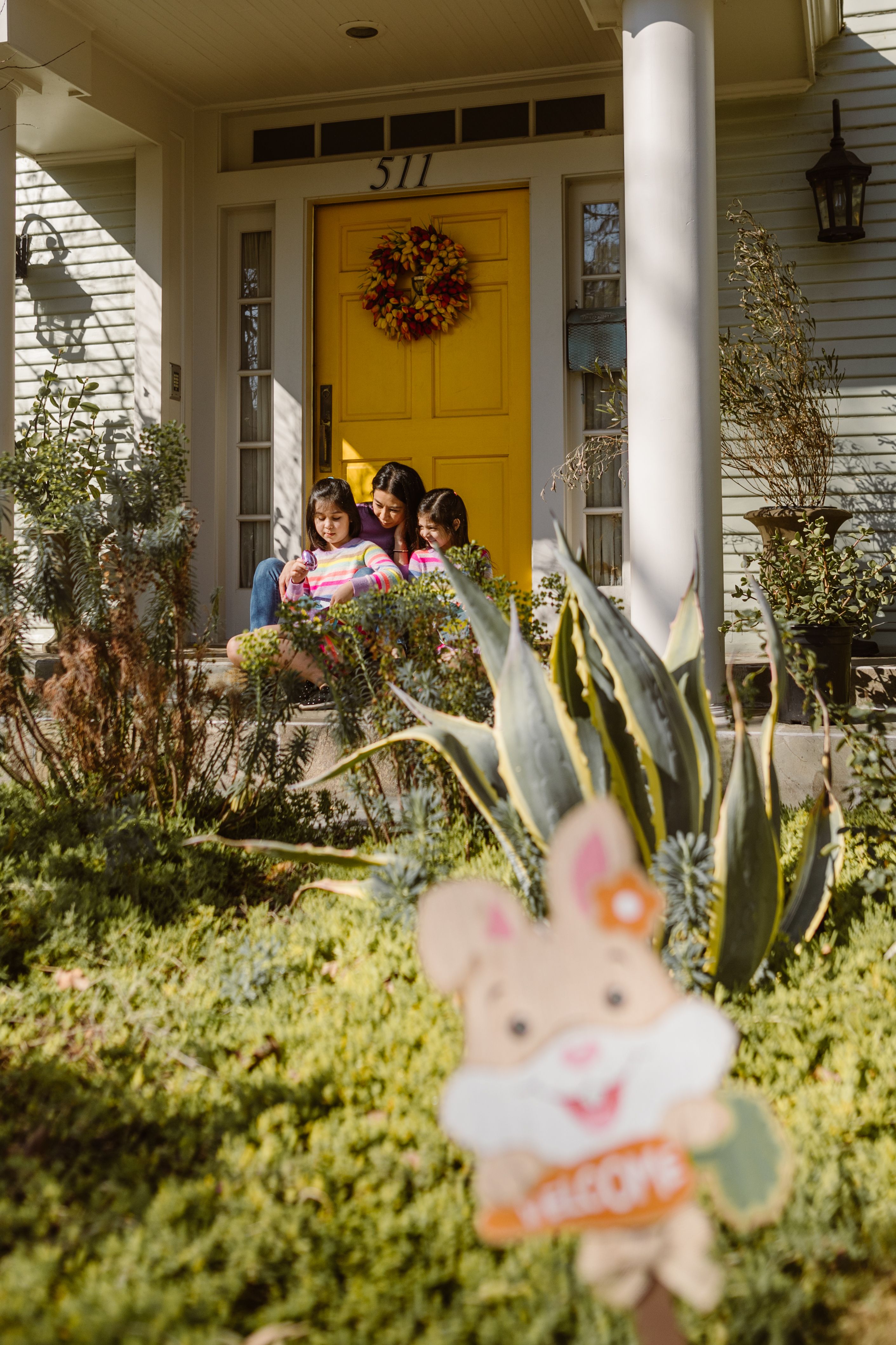 A mother and her daughters enjoy Easter together on their porch, featuring a vibrant yellow door.