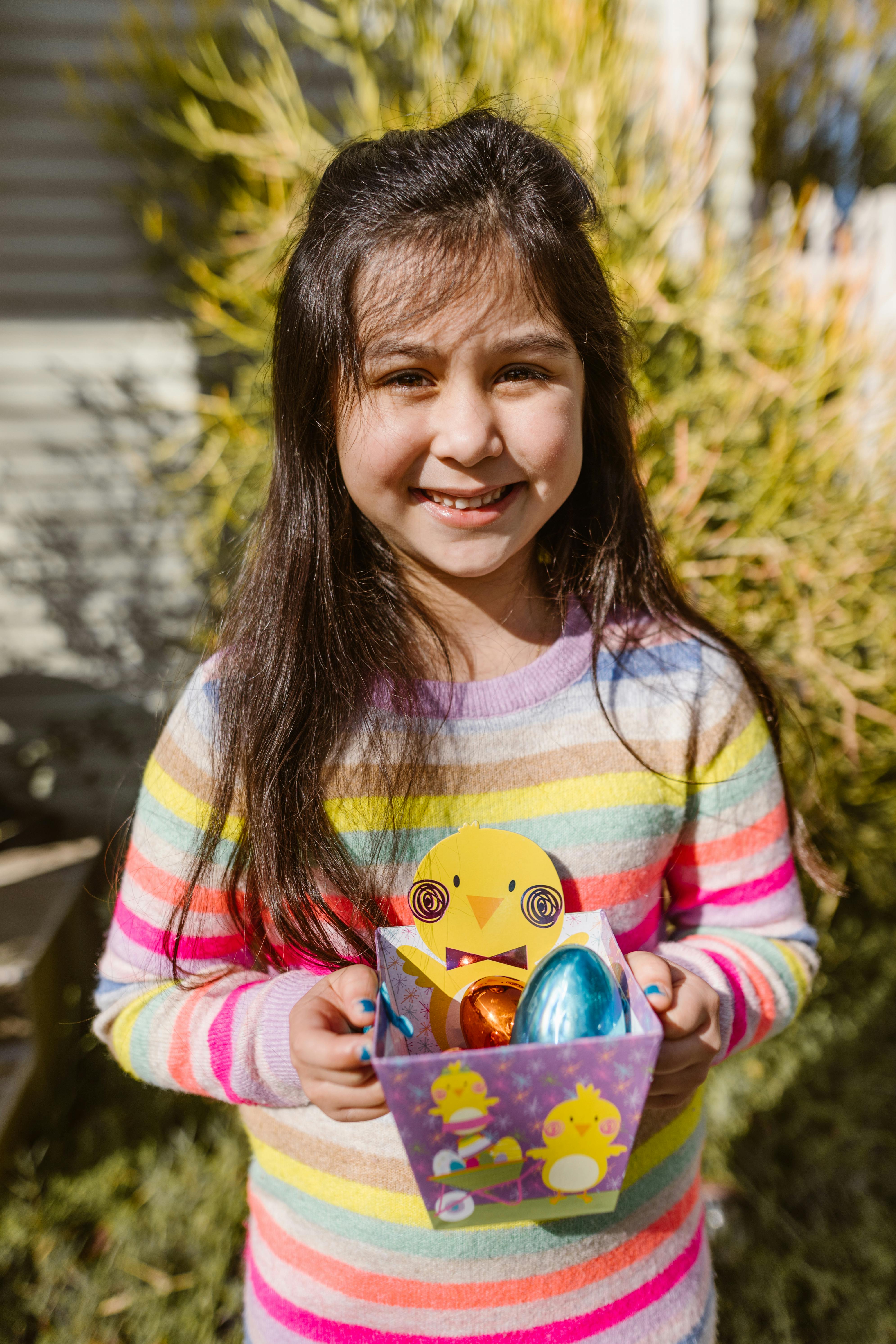 Happy girl holding colorful Easter basket on a sunny spring day.