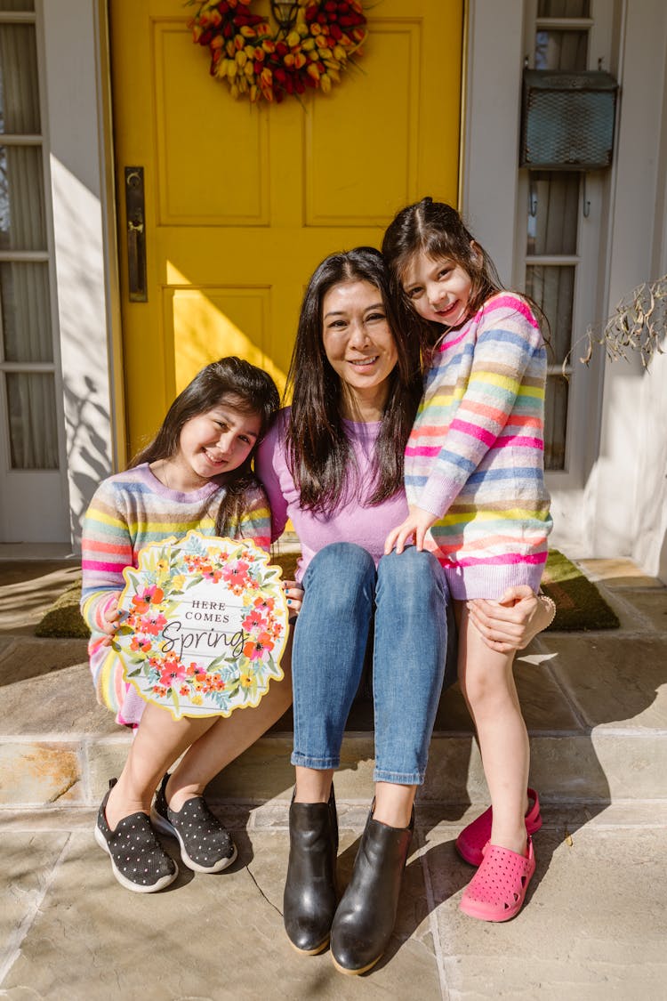 Mother And Two Daughters Sitting Outside The Front Door