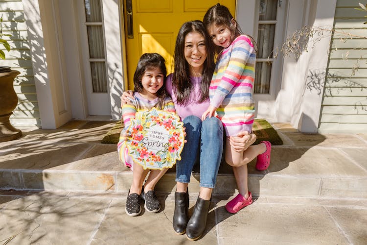 Mother And Two Daughters Sitting Outside The Front Door