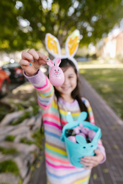 Free A young girl dressed for Easter holds a pink bunny-themed egg outdoors. Stock Photo