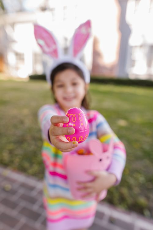 Free Smiling girl with bunny ears holding a decorated Easter egg outdoors. Stock Photo