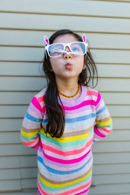 Free Whimsical child in striped dress wearing bunny-themed eyeglasses, pouting. Stock Photo