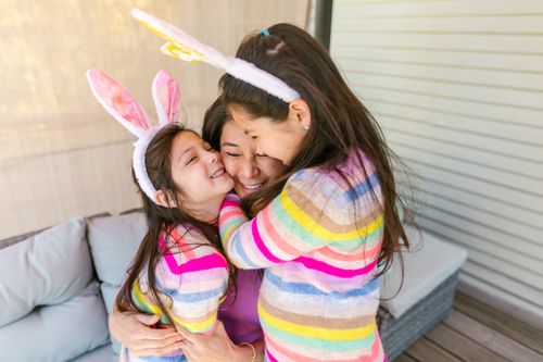 Free A mother embraces her daughters wearing colorful stripes and bunny ears, symbolizing warmth and love. Stock Photo