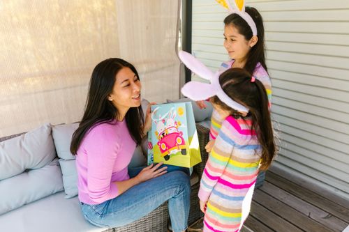 Free A joyful mother with her daughters wearing bunny ears, celebrating Easter indoors with colorful gifts. Stock Photo