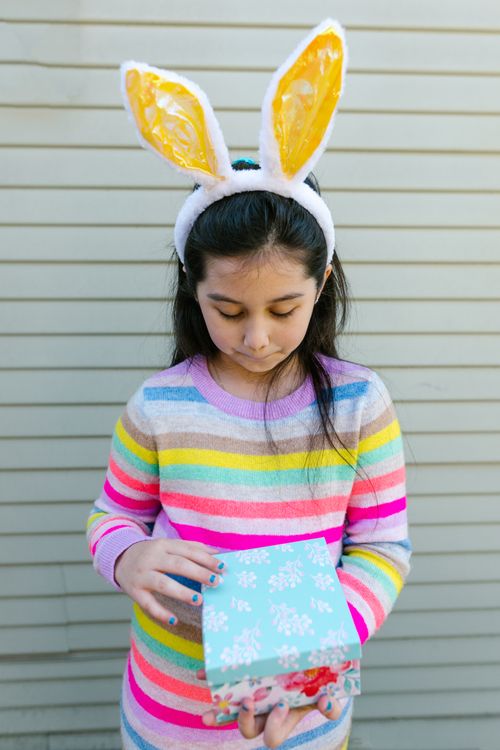 Free A young girl in a striped sweater with bunny ears holding a patterned gift box. Stock Photo
