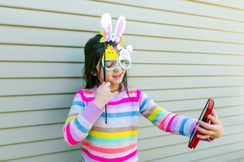 Free Cheerful girl in colorful sweater taking a playful Easter selfie with bunny props. Stock Photo