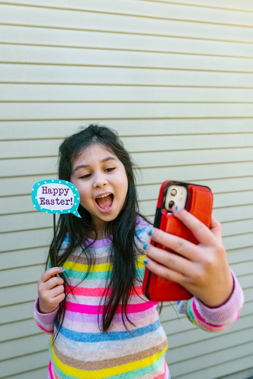 Free A cheerful girl taking a selfie with 'Happy Easter' sign outdoors. Bright and colorful vibe. Stock Photo