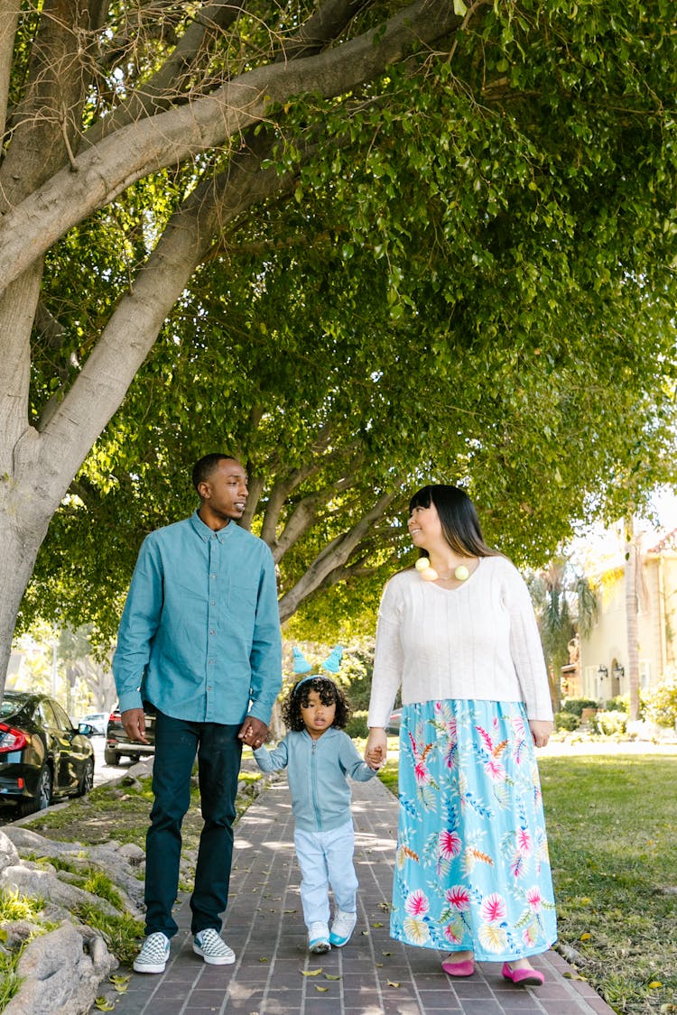 A Family Holding Hands While Walking On The Sidewalk