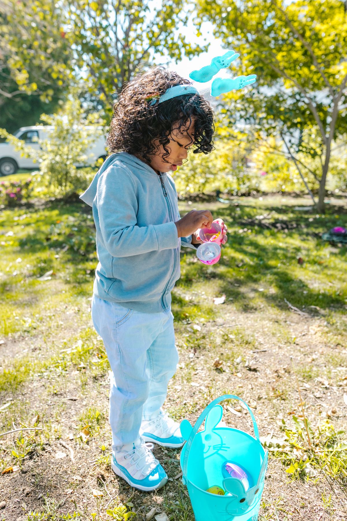 A child in bunny ears collecting Easter eggs outdoors
